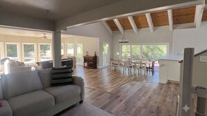 A spacious living area with a high ceiling, wooden beams, a dining area with chairs, and a kitchen with white cabinets. - Waterfront POOL with 4100 sqft home in the Country. Fish too! (Millville)
