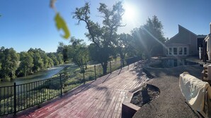 A wooden deck with a river view, a fenced area, and a house with large windows. - Waterfront POOL with 4100 sqft home in the Country. Fish too! (Millville)