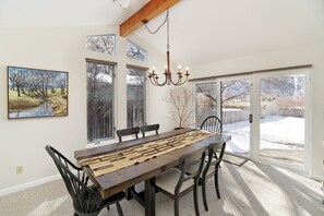 Ein Esszimmer mit Holztisch, Stühlen und einer Chandelier. Große Fenster bieten Blick auf einen verschneiten Hof.