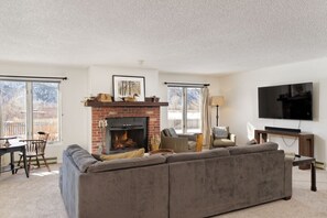 A living room with a fireplace, a sofa, a TV, and a dining area with chairs. - Carbondale Creekside Rancher - Fishing Access (Carbondale)
