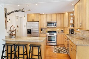 A modern kitchen with wooden cabinets, stainless steel appliances, a granite countertop, and a bar stool area. - Carbondale Creekside Rancher - Fishing Access (Carbondale)