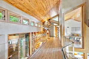 A modern interior with a wooden ceiling, a stone wall, a glass railing, and a staircase. - #1 Celebrity Mansion Estate Huge Dance Floor &  Pool Pickleball Secret Speakeasy (East Stroudsburg)