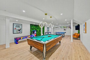 Ein Billardtisch mit grüner Spielvliesbahn, ein farbenfroher Billardqueh und ein Poster an der Wand.