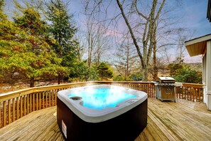 Un jacuzzi en una terraza de madera con una parrilla y árboles al fondo.