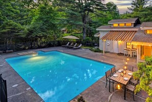 Ein Garten mit Swimmingpool, Sitzgelegenheiten im Freien und einem Haus mit überdachter Terrasse.