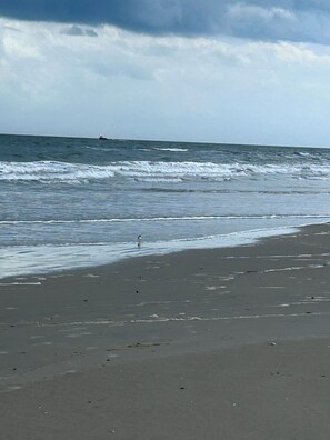Ein Strand mit Wellen, einem entfernten Boot und einem bewölkten Himmel.
