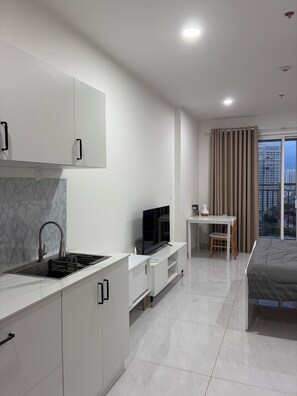 Eine moderne Küche mit integriertem Fernseher, ein Essbereich mit Tisch und Stühlen sowie ein Bett mit Blick auf die Stadt.