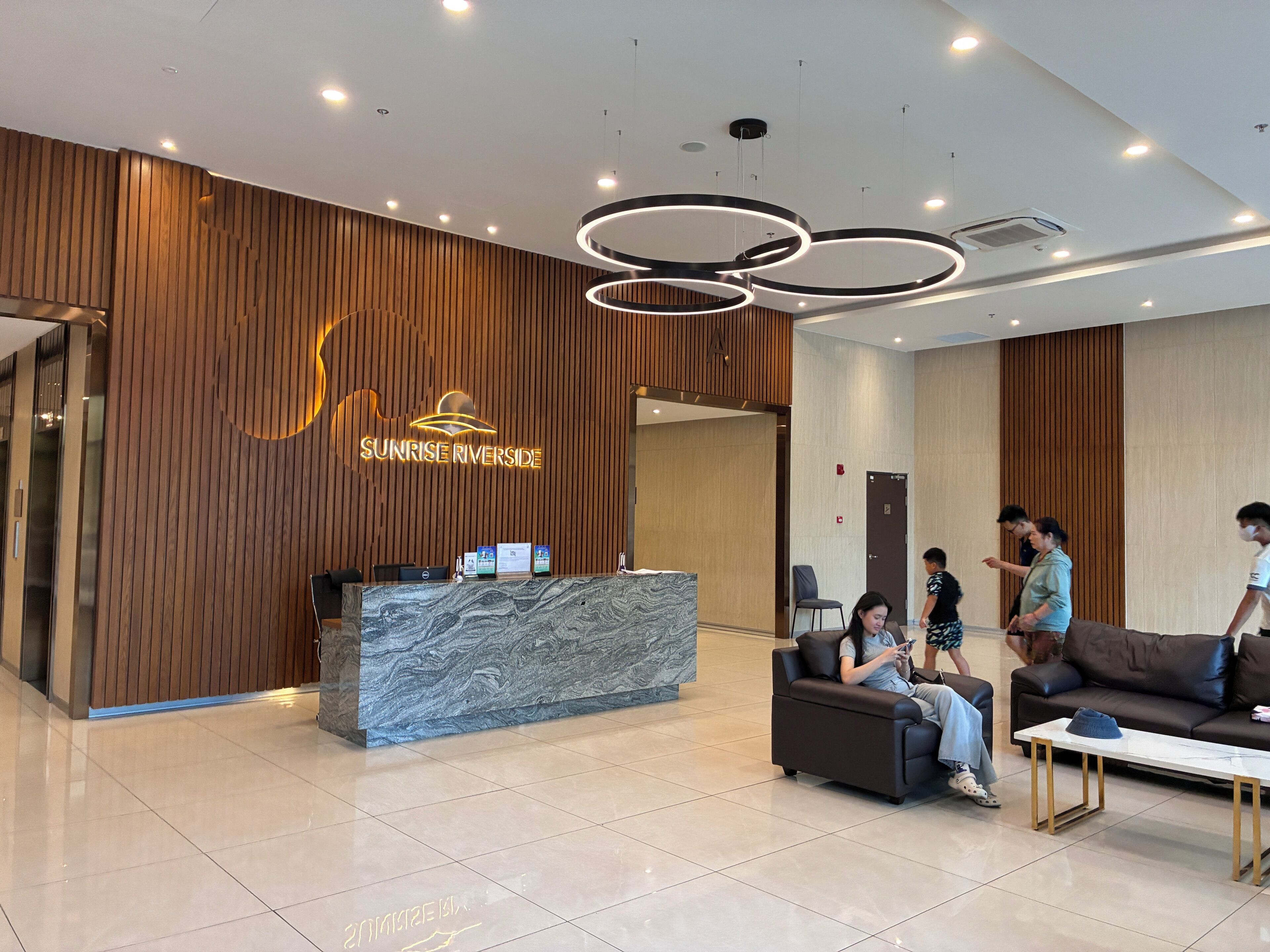 A modern reception area with a wooden wall, a marble reception desk, and a seating area with a sofa and a coffee table.