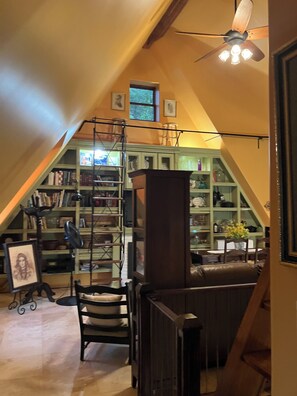 Eine Bibliothek mit Bücherregalen, einem Schreibtisch, Stühlen und einem Deckenventilator.