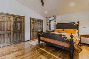 Ein Schlafzimmer mit Holzboden, einem Bett mit dunklem Kopfteil, einem Nachttisch und einem Fenster mit Vorhängen.
