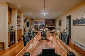 Un comedor con una larga mesa de madera, sillas, un jarrón con flores y una chimenea.