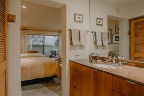 Habitación de hotel con cama, baño con lavamanos y espejo, y vista al exterior.