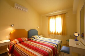 Ein Schlafzimmer mit zwei Betten, einem Schreibtisch, einem Stuhl, einem Spiegel und einem Fenster mit Vorhängen.