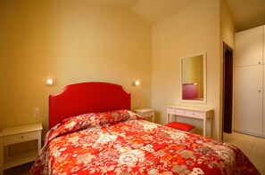 Ein Schlafzimmer mit einem roten Bett, einem weißen Schreibtisch, einem Spiegel und einem Kleiderschrank.