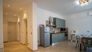 A modern kitchen with a refrigerator, stove, and dining area. - GuestHost - Ezilde Residence Flat with Parking (Quarto)