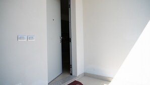 A hallway with a door leading to a room, a light switch, and a red mat on the floor. - GuestHost - Ezilde Residence Flat with Parking (Quarto)