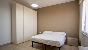A bedroom with a bed, a wardrobe, a bedside table, and a window. - GuestHost - Ezilde Residence Flat with Parking (Quarto)