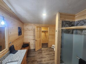 Ein Holzinnenraum mit Dusche, Waschbecken und einer Tür zu einem anderen Raum.