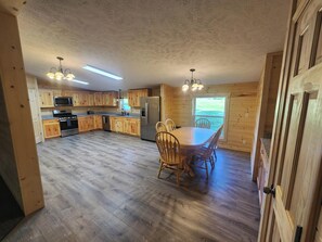 A spacious kitchen with wooden cabinets, a dining table with chairs, and a refrigerator. - 4 bed/2 bath on Conneaut Creek w/ Movie Theater, Fire Pit, Grill, A/C & More (Kingsville)