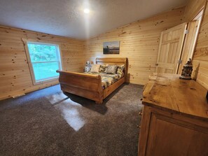 Ein Zimmer mit Holzwänden, einem Bett, einem Fenster, einem Gemälde und einem kleinen Tisch.