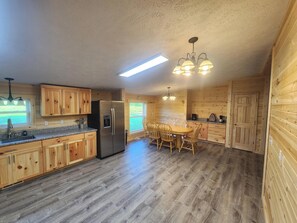Eine Küche mit Holzschränken, einem Kühlschrank, einem Esstisch mit Stühlen und einer Deckenleuchte.