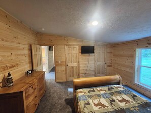 A wooden-paneled room with a bed, dresser, and a television mounted on the wall. - 4 bed/2 bath on Conneaut Creek w/ Movie Theater, Fire Pit, Grill, A/C & More (Kingsville)