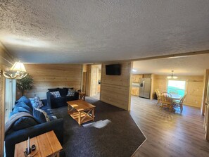 A log cabin interior with a living room, dining area, kitchen, and a TV mounted on the wall. - 4 bed/2 bath on Conneaut Creek w/ Movie Theater, Fire Pit, Grill, A/C & More (Kingsville)