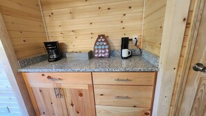 Interno di una baita in legno con un bancone della cucina, una macchina da caffè, una tazza e un oggetto decorativo.