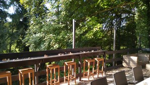 Una veranda esterna con mobili in legno, tra cui sedie e un tavolo, circondata da una recinzione e alberi.
