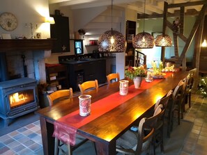 Un'area pranzo con un lungo tavolo in legno, sedie, un caminetto, lampade a sospensione e una scala.