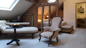 Una stanza con soffitto alto, travi in legno, un lucernario, un divano, una poltrona, un tavolino e un letto.