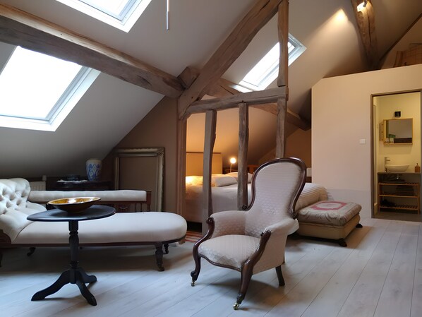 Una stanza con soffitto alto, travi in legno, un lucernario, un divano, una poltrona, un tavolino e un letto.