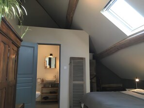 Una camera da letto con una finestra a lucernario, un letto, un comodino e un tavolino di fianco al letto.