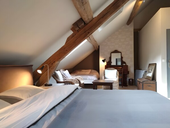 Una camera da letto con soffitto a falde, un letto, una sedia, un tavolino, una cassettiera e uno specchio.