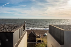 A beach view from a building with a sloped roof, a small wooden structure, and a pebble beach.
