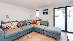 A modern living room with a sectional sofa, a floor lamp, and a painting on the wall. - Stylish Townhouse with Panoramic Sea Views | Near Beach, Canal & High Street (Hythe)