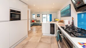 A modern kitchen with built-in appliances, a central island, and a dining area with a view. - Stylish Townhouse with Panoramic Sea Views | Near Beach, Canal & High Street (Hythe)