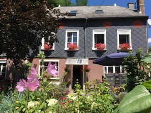 Un edificio a due piani con facciata scura, infissi bianchi e fioriere al piano superiore.