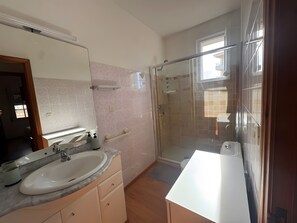Casa de banho moderna com um espelho grande, uma pia, um chuveiro e área de duche com divisória de vidro.