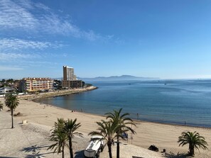Um hotel à beira-mar com vista para a praia, zona de estacionamento e céu limpo.