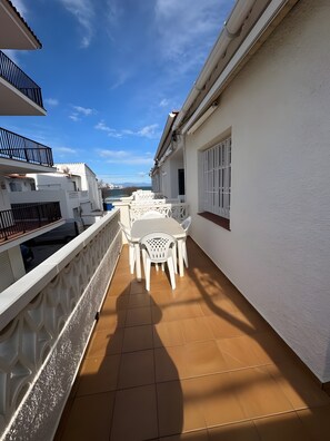 Uma varanda com cadeiras e mesa de plástico branco, paredes brancas e chão de azulejos.