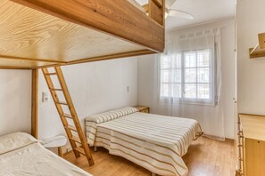 Una stanza con un letto a castello, una scala, una scrivania piccola e una finestra con tende.