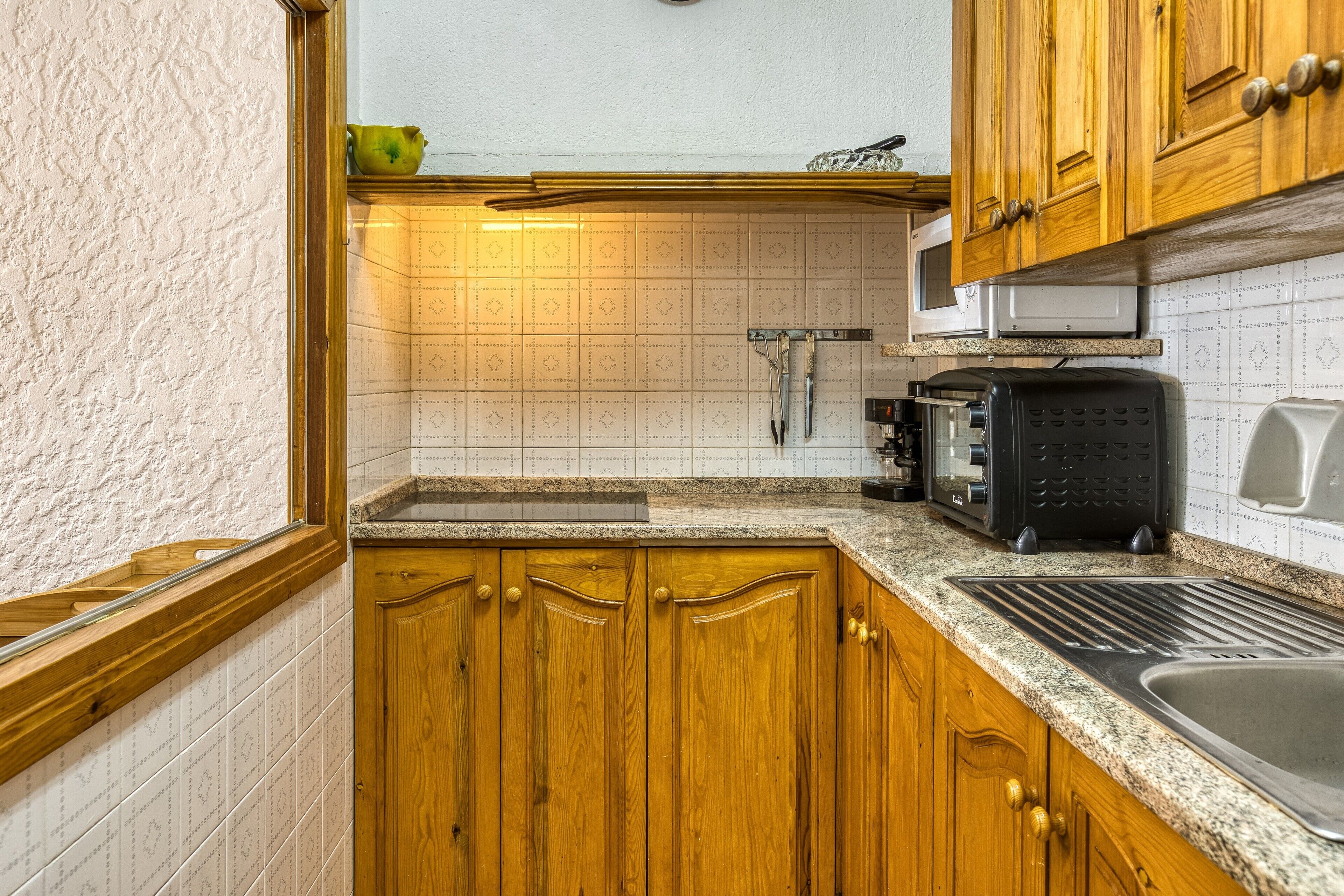 Una cocina con armarios de madera, un microondas, un tostador y un lavabo.