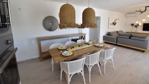 Uma sala de jantar com mesa de madeira, cadeiras brancas e luminárias de palha suspensas.