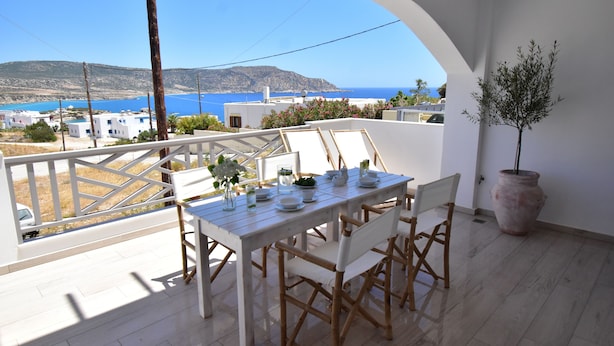 Varanda com mesa posta para refeições, com vista para a costa, edifícios e céu claro.