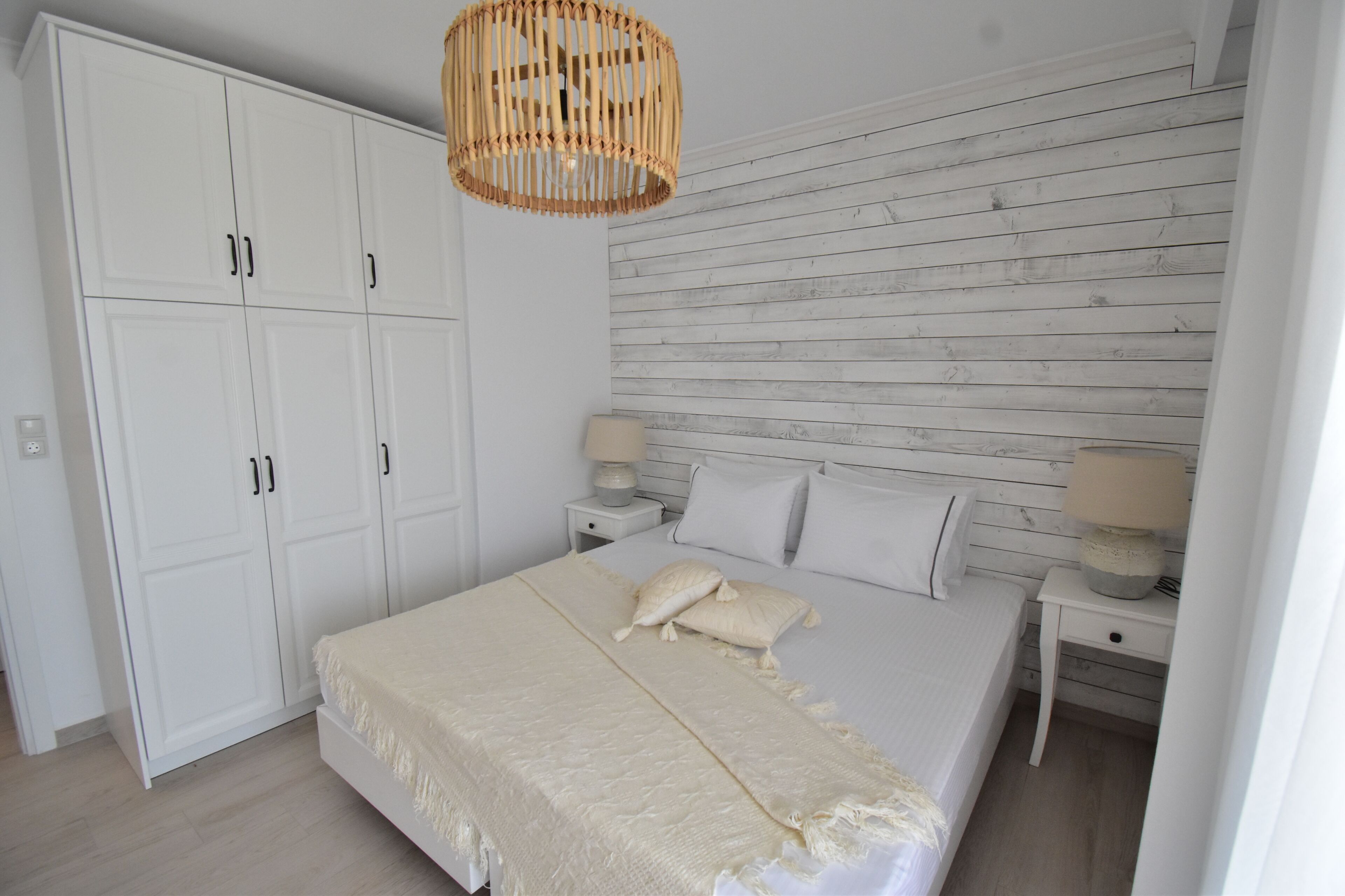 A bedroom with a bed, white wardrobe, wooden wall paneling, and two bedside lamps.