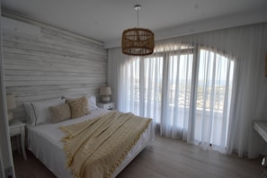 A bedroom with a bed, white curtains, a hanging light fixture, and a view through the window. - Harmony Villa 2 (Karpathos)