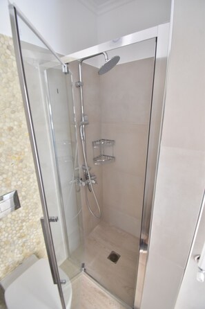 Een douchecabine met glazen wanden, een handdouche, een wandrek voor handdoeken en een klein plankje.