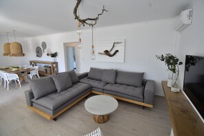 Een moderne woonkamer met een hoekbank, een ronde salontafel en een eethoek met een houten tafel en witte stoelen.