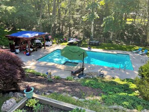 A backyard with a swimming pool, a covered patio area, and a garden.
